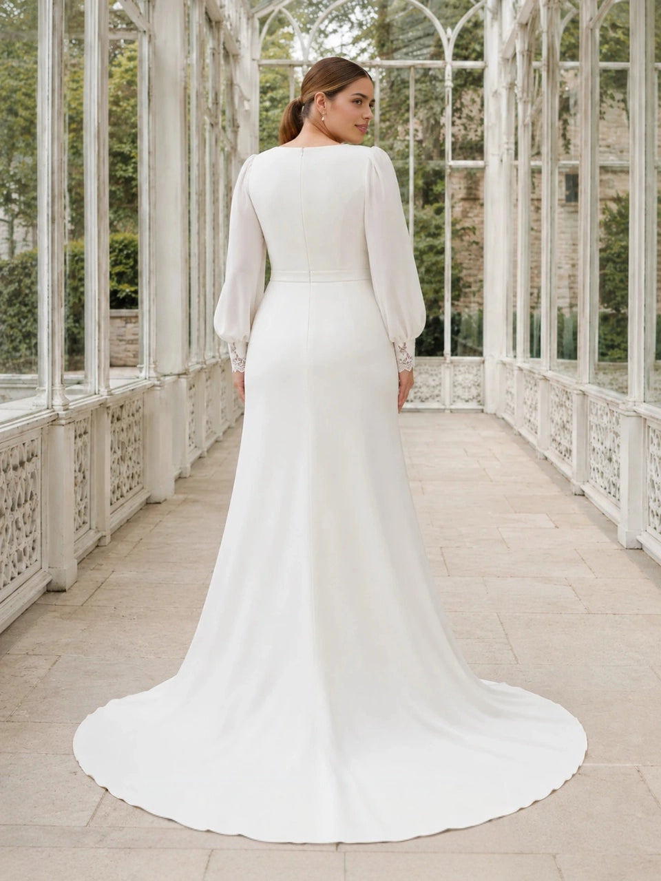 Back view of an ivory plus size wedding dress with long bishop sleeves, lace cuffs, a center zipper and chapel train.