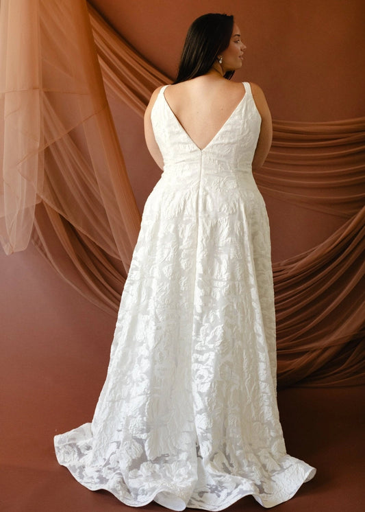 Ivory plus size floral wedding dress featuring deep V-back, center zipper closure, fitted waist and flowing A-line skirt with soft train