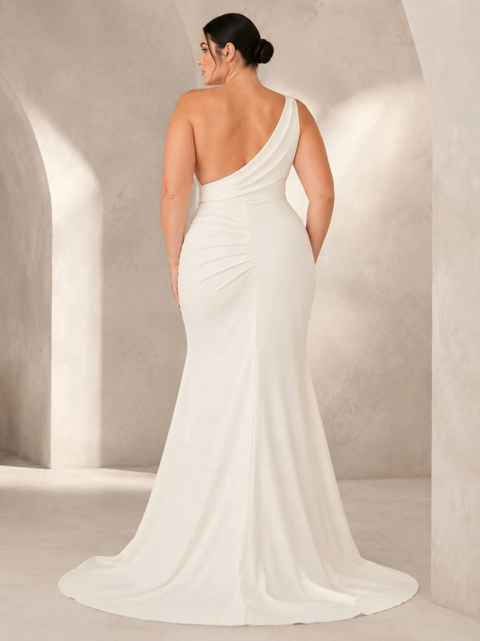 Back view of ivory plus size wedding dress featuring an asymmetric open back, diagonal shoulder strap and flowing train.