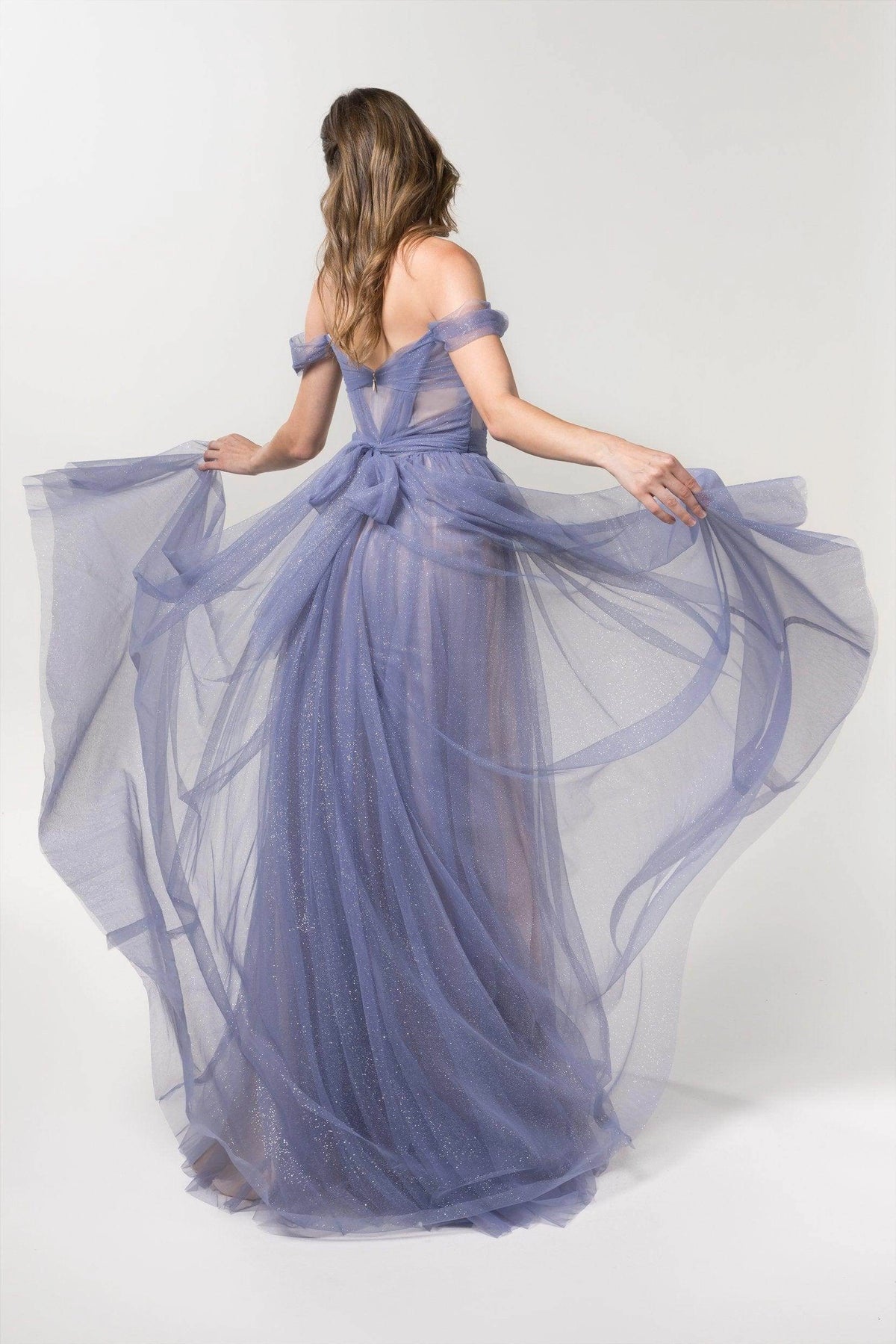 Back view of Roselledress periwinkle bridesmaid dress with a low V back, waist bow, sheer bodice panels and flowing shimmer tulle skirt.