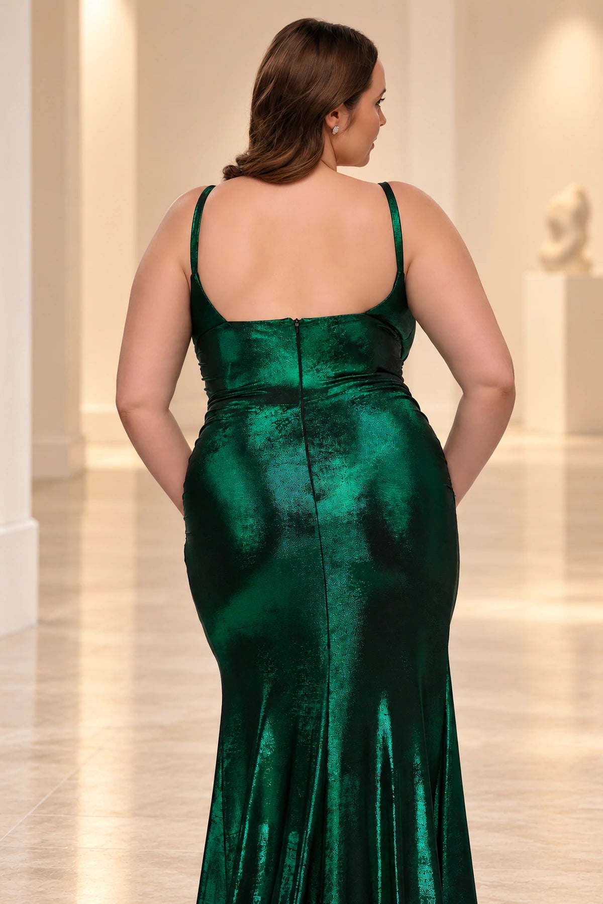 Back detail of an emerald green metallic prom dress showing slim straps, a low square back, center zipper and waist ruching.