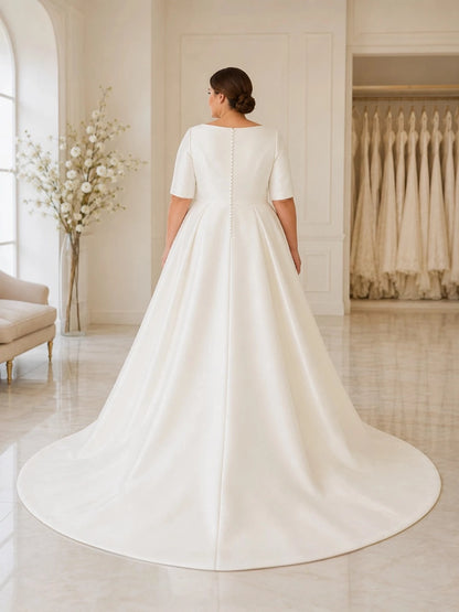 Back view of ivory plus size wedding dress with square back, covered button details, short sleeves and a sweeping satin skirt.