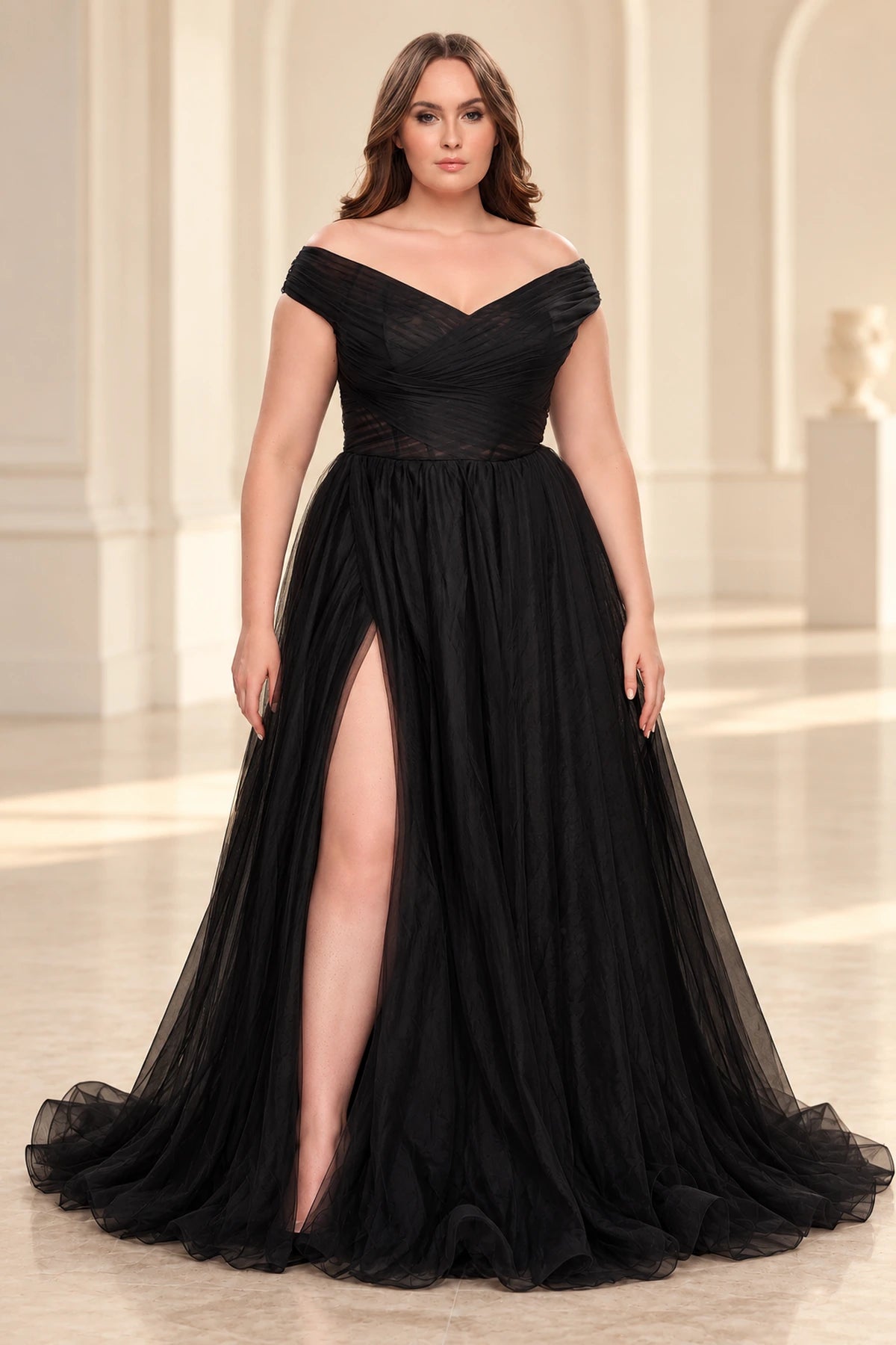 Front view of a black tulle A-line prom dress with an off-shoulder V-neck, crossover ruched bodice, sheer waist and high slit.