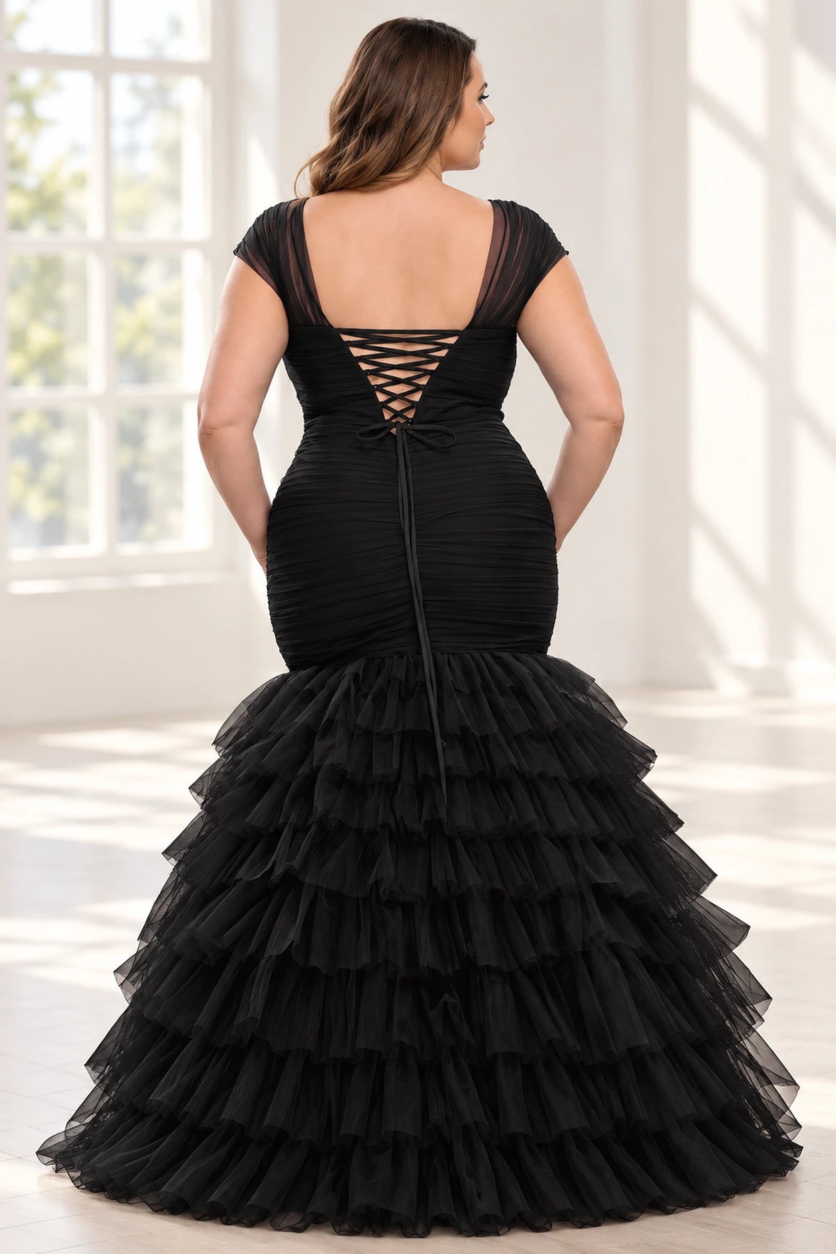Back view of a black tulle mermaid evening dress featuring a low scoop back, crisscross lace-up ties and a tiered ruffle skirt.