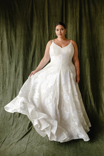 Ivory plus size A-line wedding dress with V-neckline, spaghetti straps, floral textured fabric and flowing floor-length skirt front view