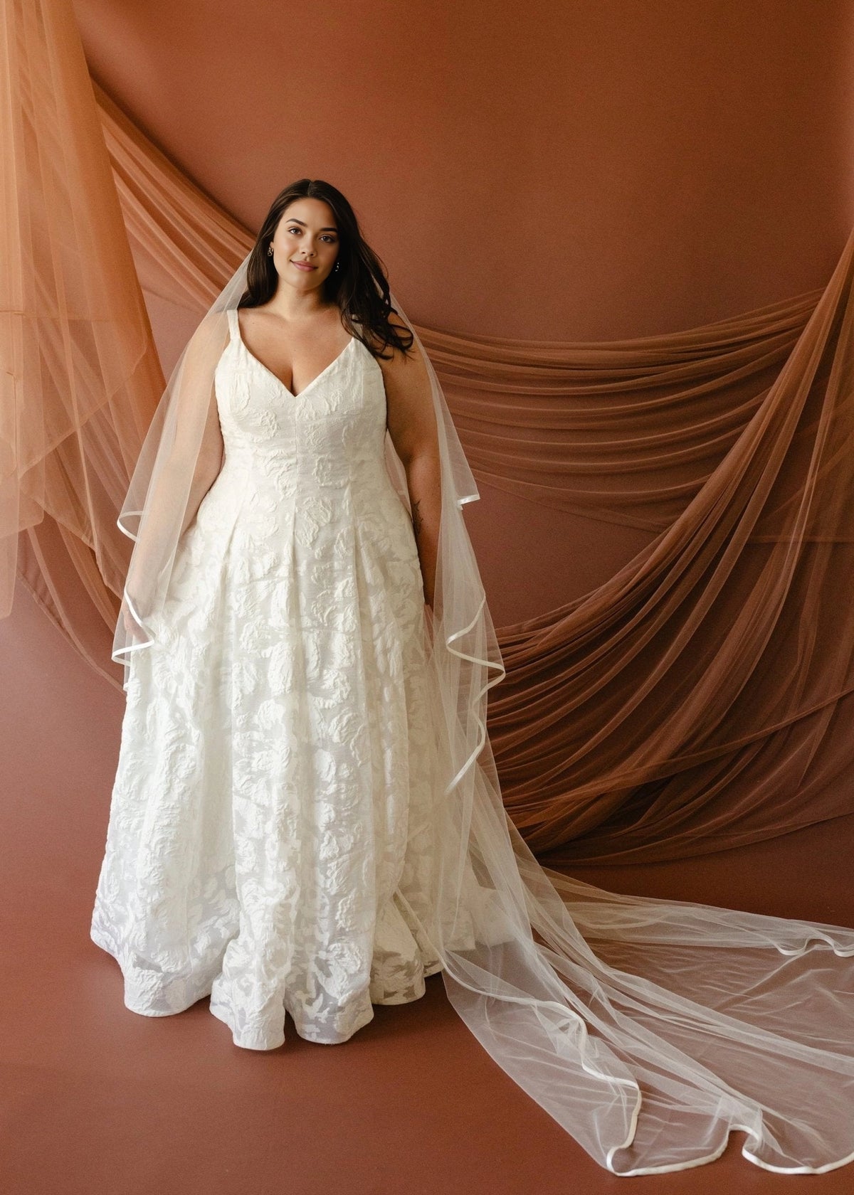 Ivory plus size A-line wedding dress with V-neckline, wide shoulder straps, floral textured fabric and flowing floor-length skirt front view