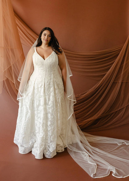 Ivory plus size A-line wedding dress with V-neckline, wide shoulder straps, floral textured fabric and flowing floor-length skirt front view