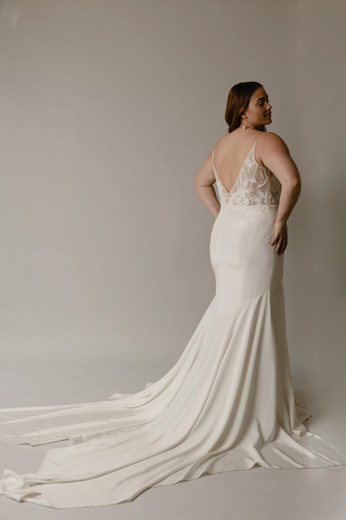 Ivory plus size mermaid bridal gown featuring deep V-back, sheer floral lace details, fitted hips and flowing long train