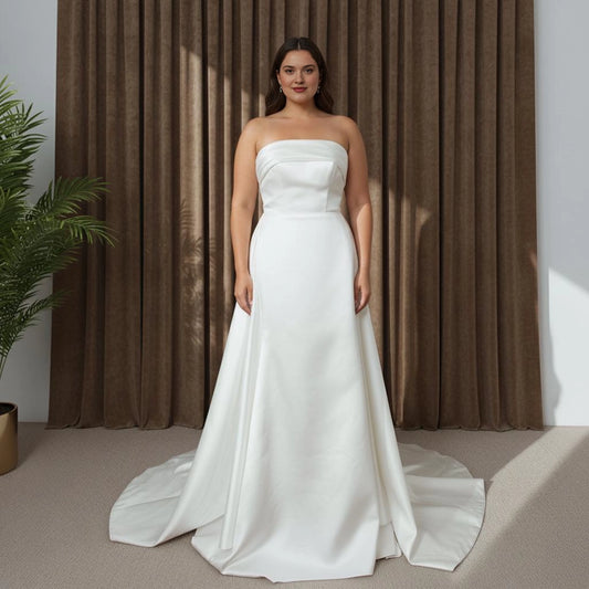 Ivory plus size wedding dress with straight strapless neckline, structured fitted bodice, sleek sheath skirt and flowing A-line overskirt