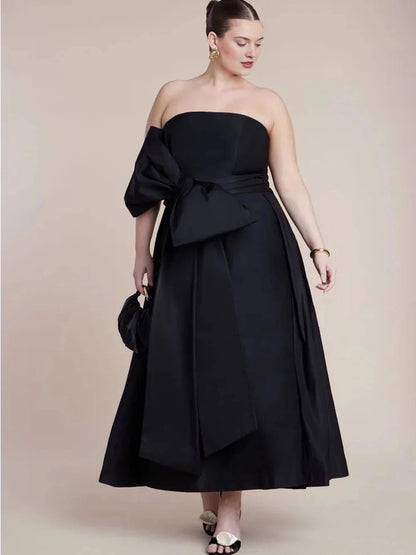 Plus size black wedding guest dress with strapless neckline, bow waist detail and elegant A-line midi skirt by roselledress.