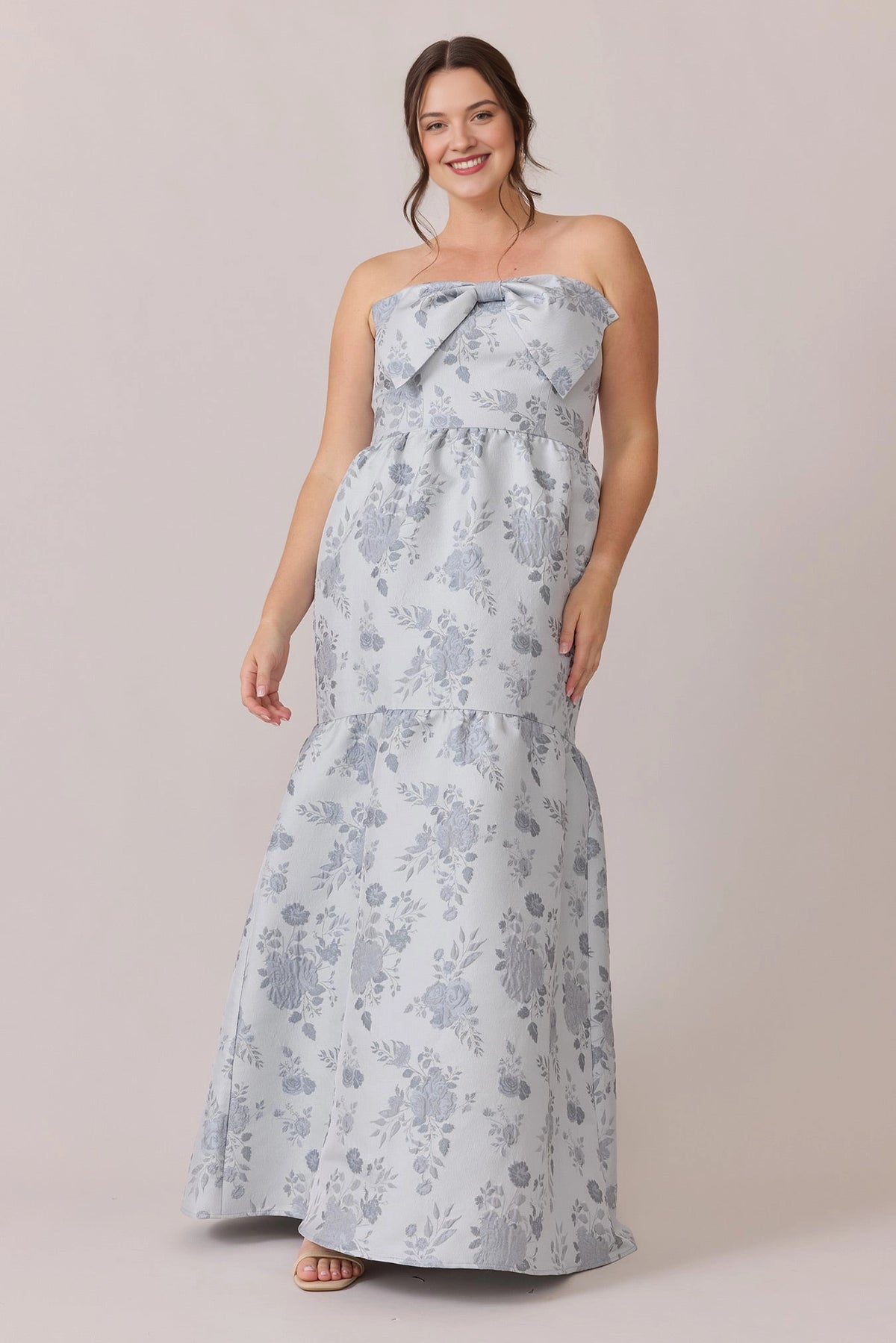 Plus size dusty blue floral jacquard strapless wedding guest dress with bow at bust, tiered ruffle skirt and lace-up back, front view
