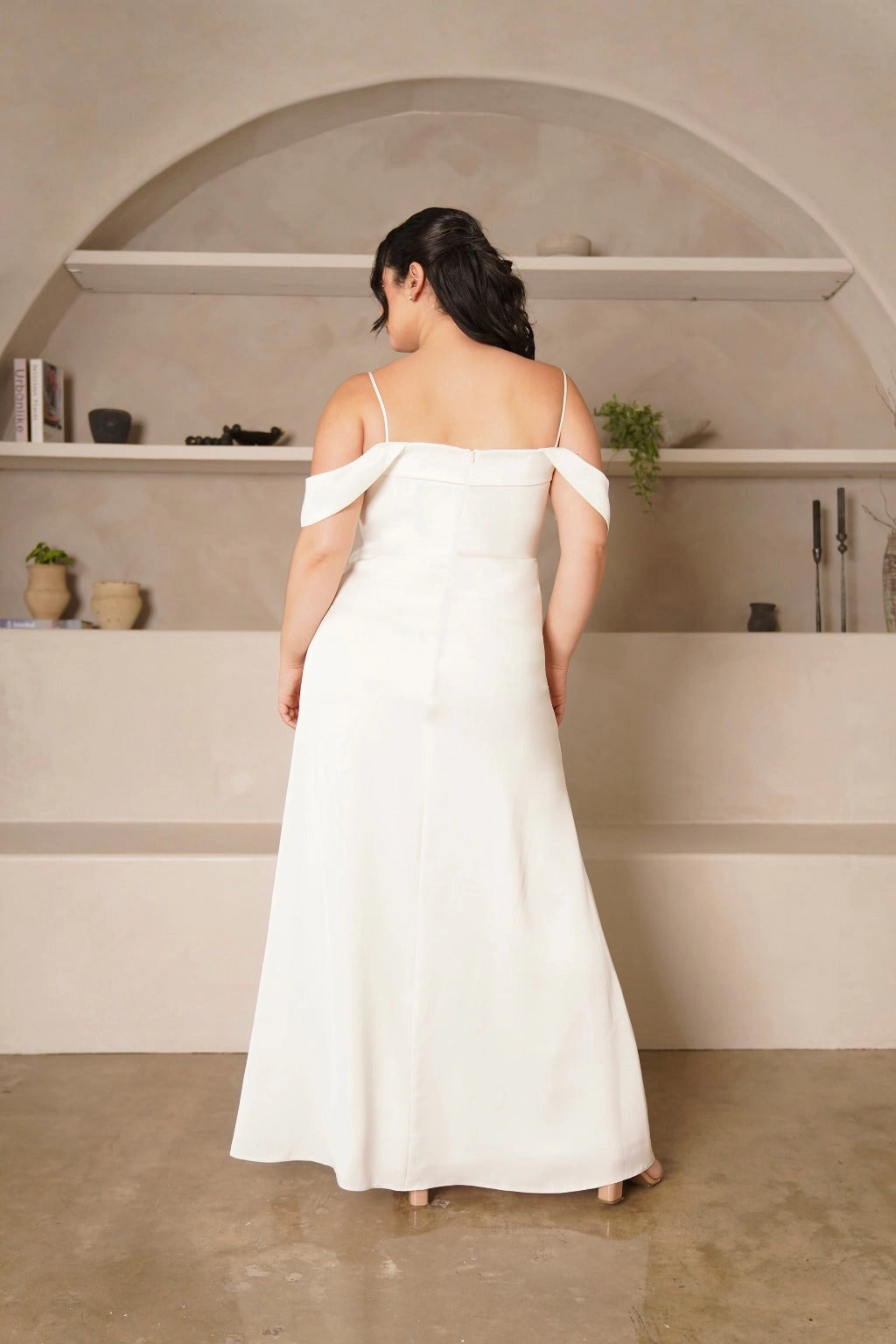 Back view of plus size ivory wedding guest dress featuring a straight back, delicate straps, draped off-shoulder sleeves, center zipper and floor-length skirt.