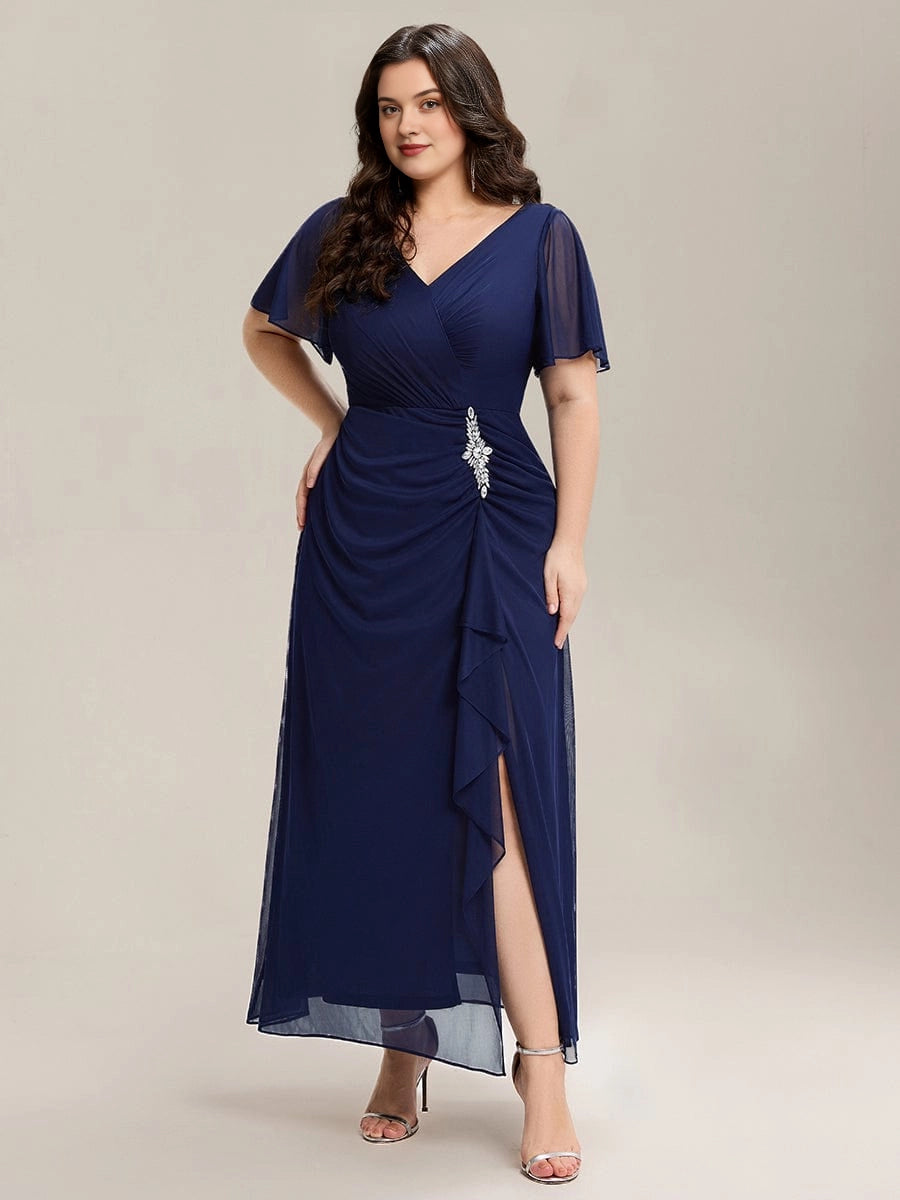 Plus size navy chiffon mother of the bride dress with V-neck wrap bodice, flutter sleeves, rhinestone brooch at waist, cascade ruffle slit and flowing long skirt, front view
