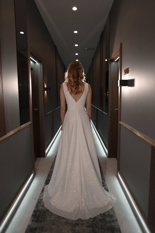 White plus size glitter wedding dress with deep V-back, center zipper closure, fitted waist and sparkling A-line skirt with sweep train