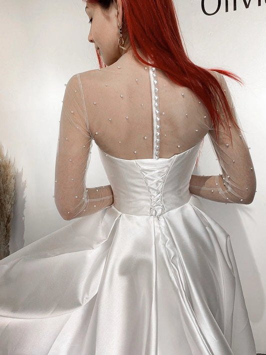 White satin-look wedding dress with lace-up corset back, pearl embellished sheer long sleeves and pleated bridal skirt
